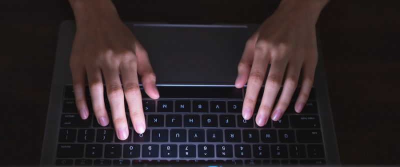 Close up of hand using computer and keyboard typing to the Internet online.